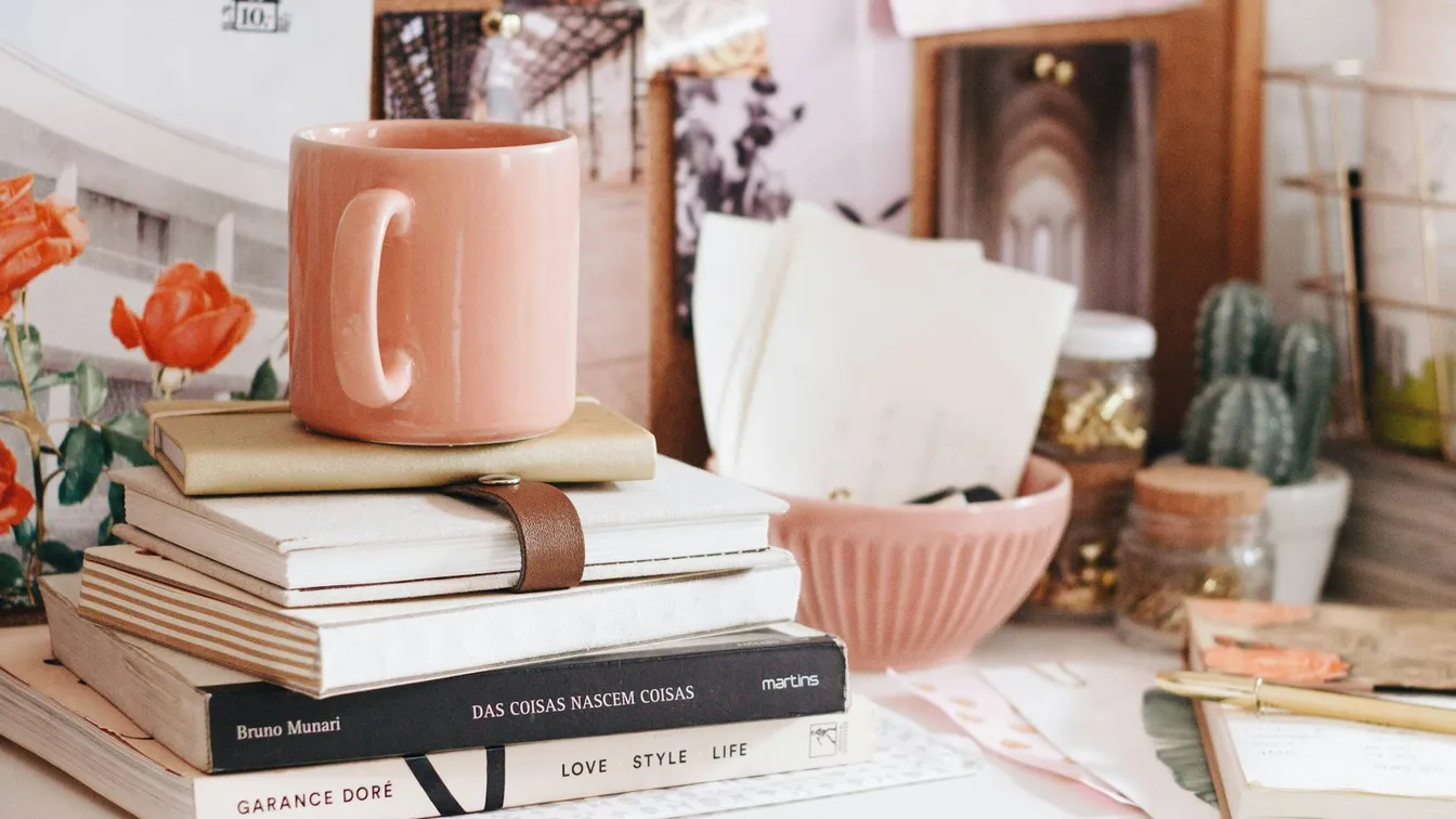 a stack of books on a desk with a pink mug