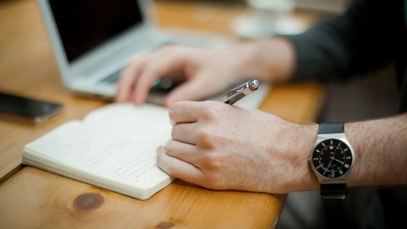 a man writing in a notebook with a watch on his wrist