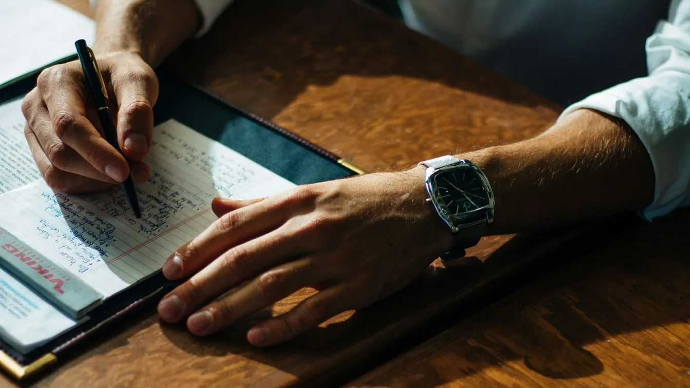 a man writing in a notebook with a watch on his wrist