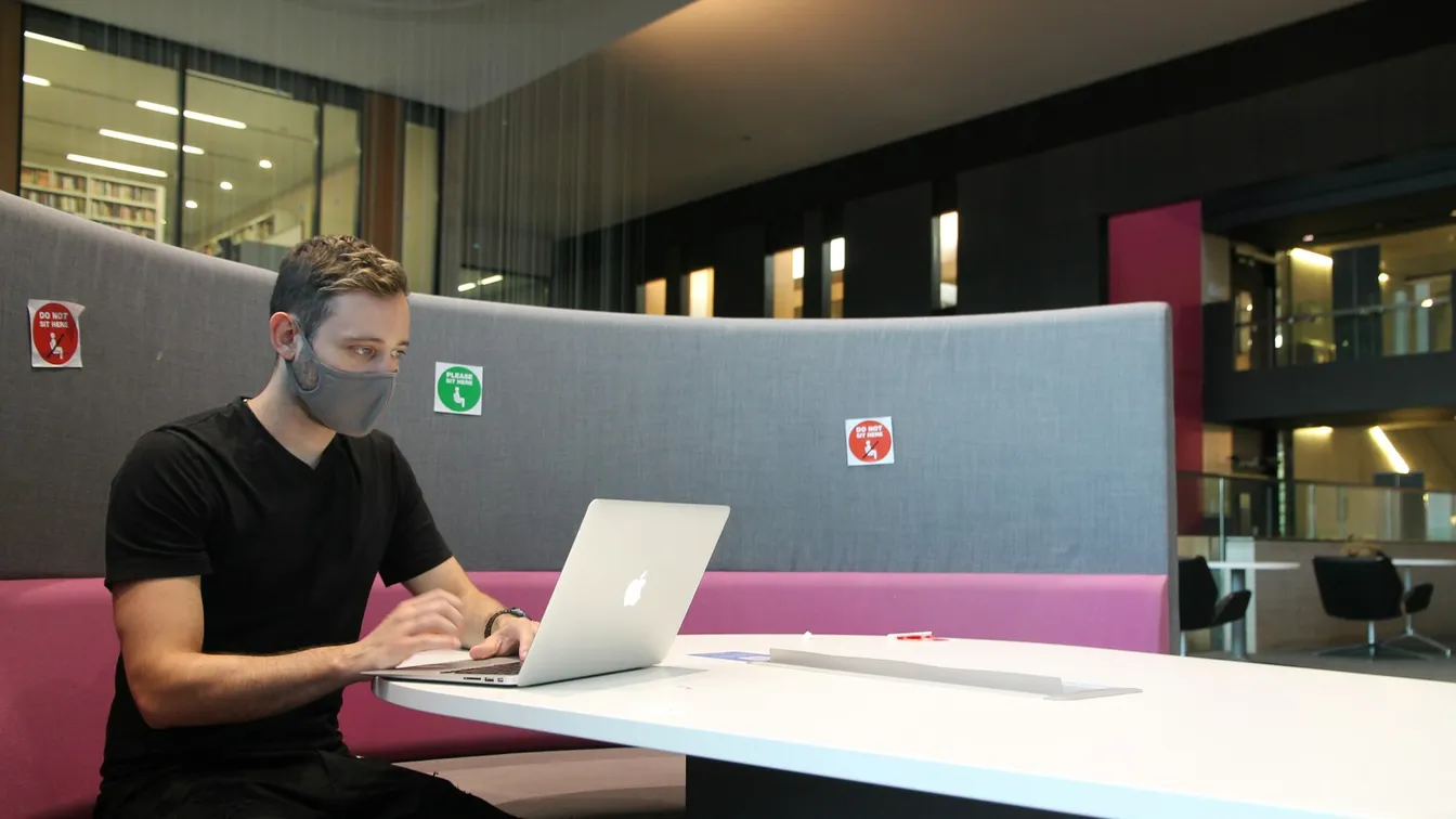 a man sitting at a desk with a laptop and a face mask