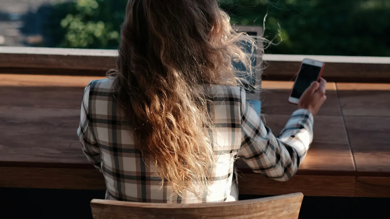 a woman sitting at a table with a laptop and a cell phone