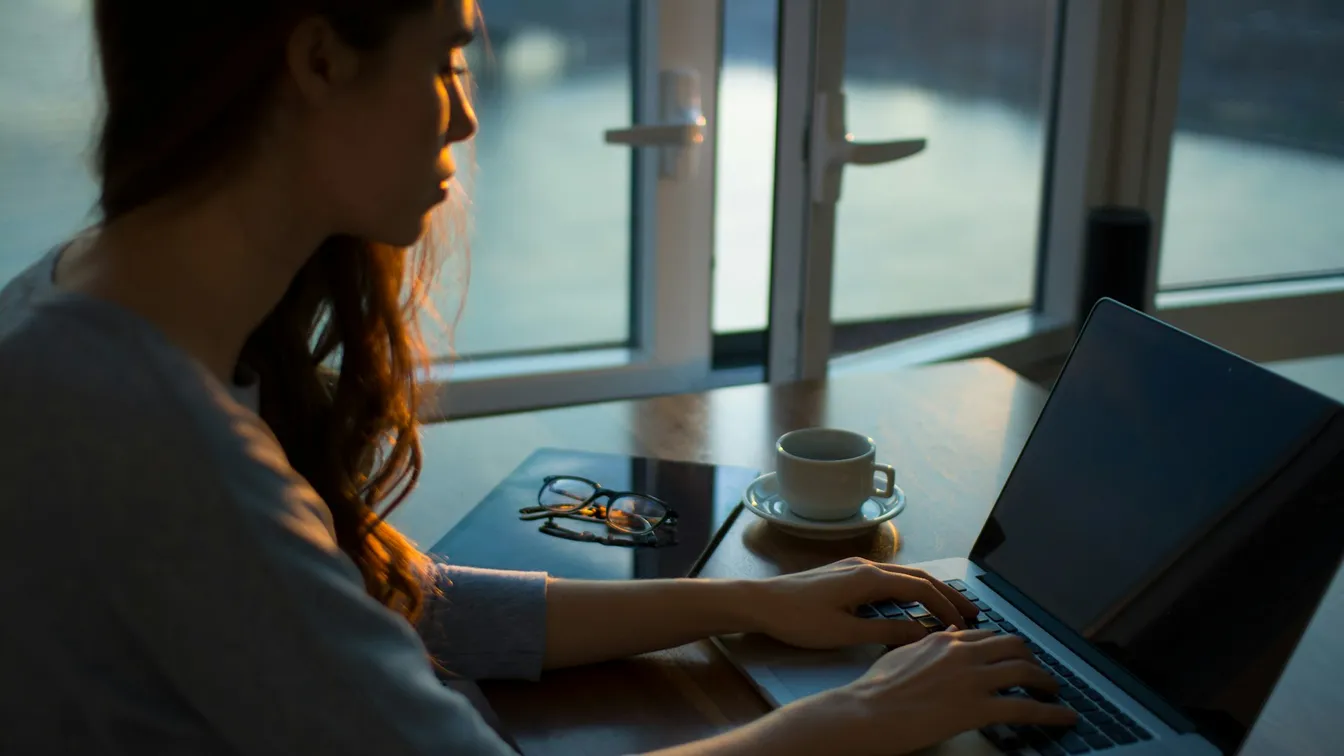 a woman is working on her laptop in front of a window