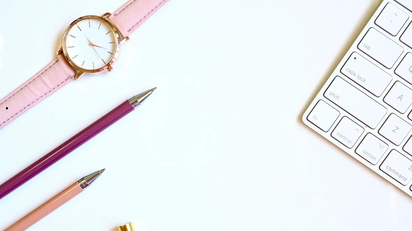 a pink watch, pencils, and a keyboard on a white table