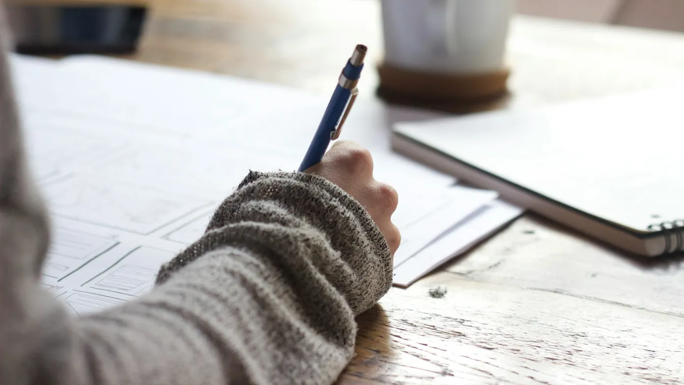 a person writing with a pen at a desk