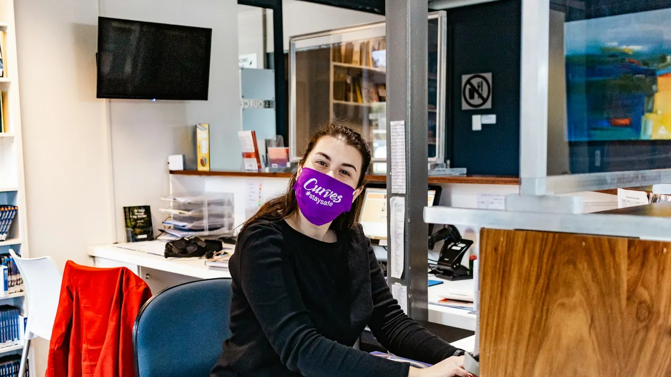 a woman wearing a purple face mask sitting at a desk